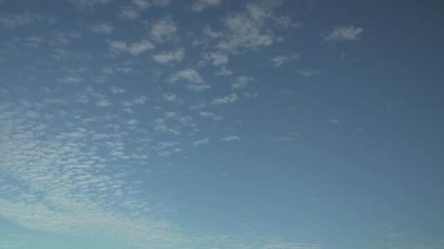Wispy cirrocumulus clouds drift slowly, creating a rhythmic mackerel sky pattern against a vast blue firmament. Ideal for weather forecasting, nature documentaries, or serene cinematic visuals. 