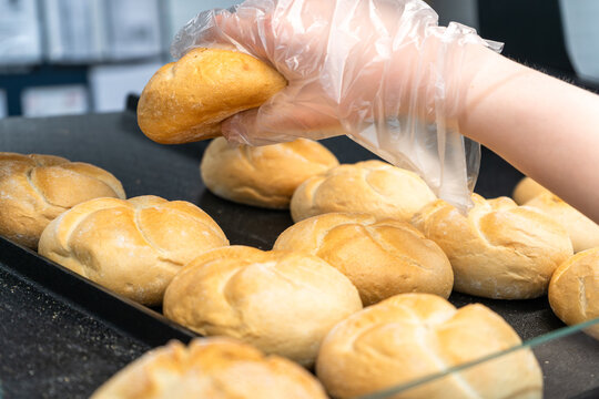 Gloved hand lifting fresh bread roll from tray in self service bakery section