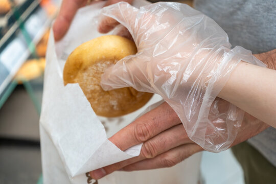 Fresh bread roll packed into paper bag by customer wearing disposable glove