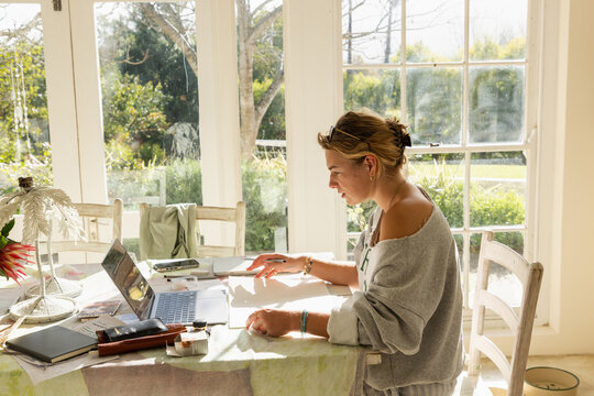 young woman artist in her studio using laptop and working on a pencil drawing