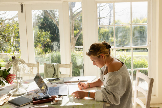 young woman artist in her studio using laptop and working on a pencil drawing