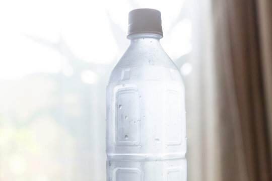 水滴がついた清涼感のある冷たいミネラルウォーターのペットボトル　熱中症対策 水分補給イメージ  室内に置かれたペットボトルの水