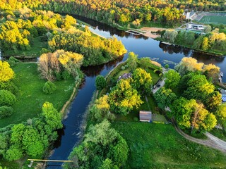Fototapeta premium Aerial drone view of a winding river through lush green forest at sunset