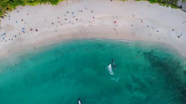 People relax on the white sand beach and swim in the clear blue ocean water beside lush jungle on Patong Beach, Phuket, Thailand during vacation