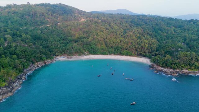 Aerial view capturing a beautiful sandy beach, tropical jungle, and clear blue ocean around Freedom beach, Phuket, Thailand during golden hour