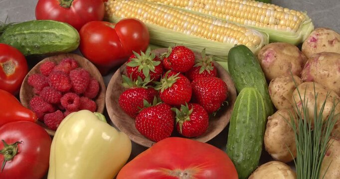 Various fresh healthy products on a gray table. Close-up footage of  corn, strawberries, cucumbers, tomatoes, green onions, potatoes, raspberries, dill, sweet peppers on a rotating table.