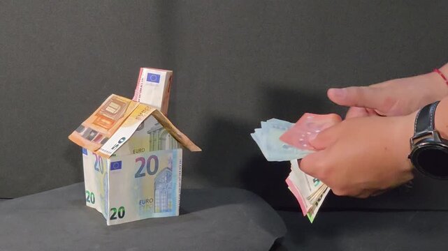 Woman showing euro banknotes fan next to a house model, dark background