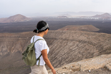 Woman hiking volcano rim, exploring volcanic landscape and craters, enjoying journey in Timanfaya National Park, Lanzarote © Alberyo
