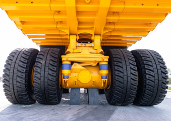 Low-angle view of the underside of a large yellow dump truck focusing on dual rear axles, heavy tread tires, suspension components and metal chassis. Bright © NastyaPhoto
