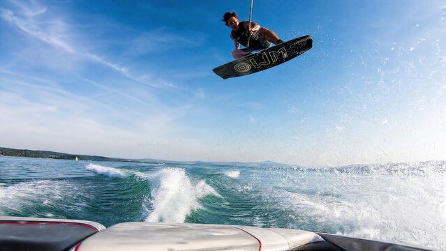 Low-angle view from a speedboat, a wakeboarder airborne against the sky.