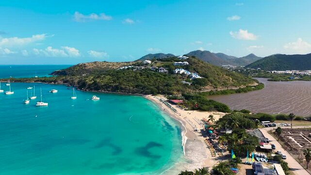Aerial view of Friar's Bay and Etang Guichard salt pond on the French side of Saint Martin island in the Caribbean. White sand beach organized with beach umbrellas, sunbeds, and people relaxing.