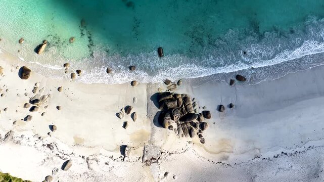 Faszinierende Drohnenaufnahme vom Plage de Boutrouilles: T&uuml;rkisblaues Wasser und wei&szlig;er Gischt-Schaum treffen auf hellen Sandstrand und markante, dunkle Granitfelsen.