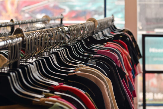 Selective focus view of women's clothing hanging on retail racks in front of a large window, showcasing apparel display and fashion shopping environment
