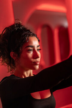 Focused Latina fitness model performing Pilates resistance training with photobiomodulation red light therapy in wellness center