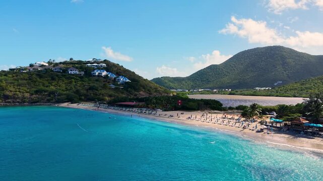 Drone view of Friar's Bay beach and Etang Guichard salt pond on the French side of Saint Martin island in the Caribbean Sea. Turquoise water gently washes the sandy shoreline near green tropical hills