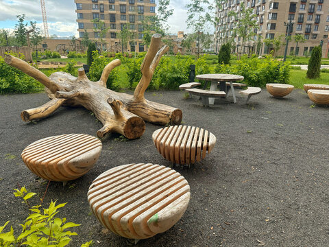 A modern eco-friendly recreation area with unique wooden benches, a large tree log, and a picnic table in a residential courtyard. Concept of eco-friendly urban landscaping 