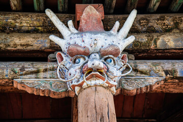 Yungang, China - May 9 2026: An intricate, weathered dragon head wood carving serves as a decorative corbel beneath the layered, tiled eaves of a multi-storied pavilion facade at the Yungang Grottoes © Vincent Jiang