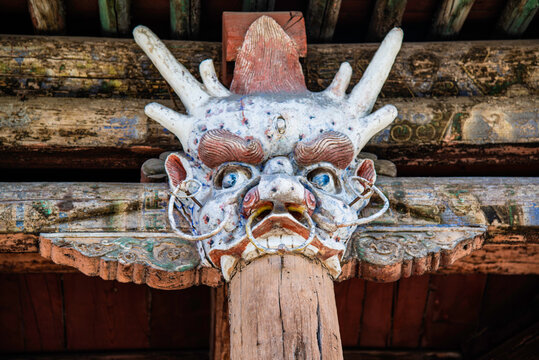 Yungang, China - May 9 2026: An intricate, weathered dragon head wood carving serves as a decorative corbel beneath the layered, tiled eaves of a multi-storied pavilion facade at the Yungang Grottoes