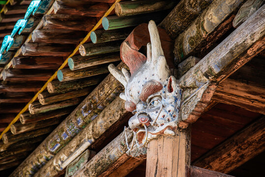 Yungang, China - May 9 2026: An intricate, weathered dragon head wood carving serves as a decorative corbel beneath the layered, tiled eaves of a multi-storied pavilion facade at the Yungang Grottoes