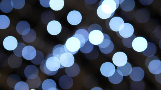 Out of focus blue and white circular lights glow across a dark background, creating an abstract festive atmosphere with soft illumination and scattered light points