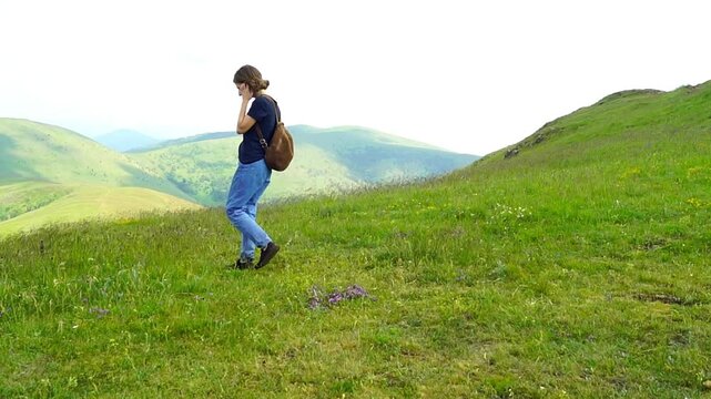 Female tourist pauses along mountain slope, shifting attention between nearby terrain and distant ridgeline scenery. Shows observational hiking, environmental awareness, and attention to landscape.