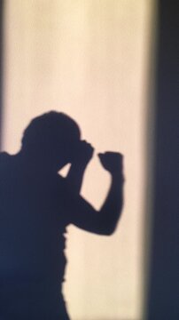 a silhouette of a man boxing against a wall, practicing a fighting stance with clenched fists