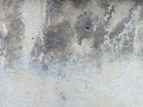 An old weathered concrete wall with a rough and porous texture. A large portion of the surface is covered in dark mold stains and patches of moss.