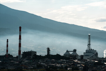 Obraz premium Industrial factory smokestack mountain fog city chimney pollution landscape plant industrial factory with smokestack near mountain slope, fog over city skyline, chimney tower, pollution haze