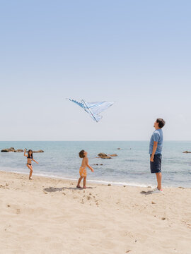 Man flying kite with his kids at beach 