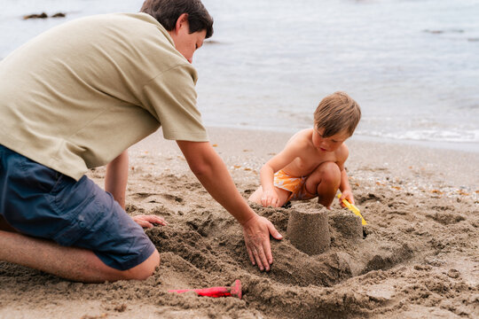 Father building sand castle with his little son at beach 