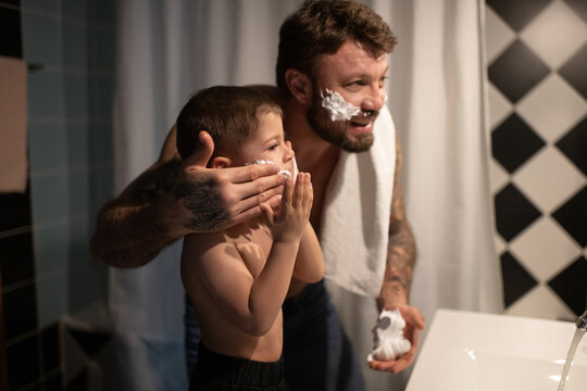 Cheerful father and son shaving faces in bathroom