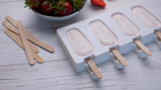 Preparing homemade strawberry popsicles for freezing