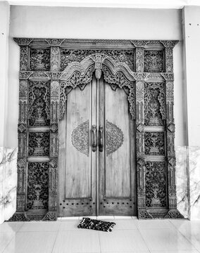 The black and white view of old wooden entrance doors, intricately carved,  entrance door with a small padlock in Ungaran, Indonesia. Selective focus.