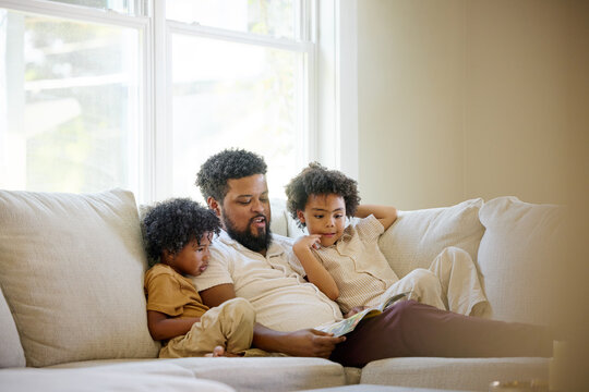 Father Reads to Children on Sofa During Daytime