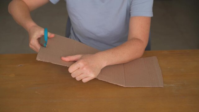 Woman cutting a piece of cardboard with scissors at a table, high quality audio recording. Firm cutting and snipping sounds. Craft process, DIY work and everyday lifestyle concept.