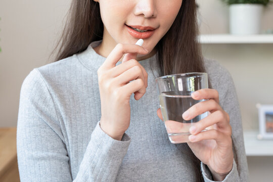 Female patient swallowing a drug tablet or vitamin supplement capsule with water for treatment at home.