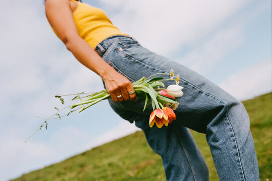 Woman walks in field while holding flowers in her hand