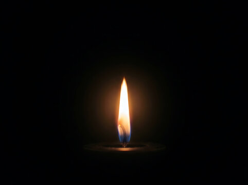 Single candle flame burning brightly against a deep black background fire light