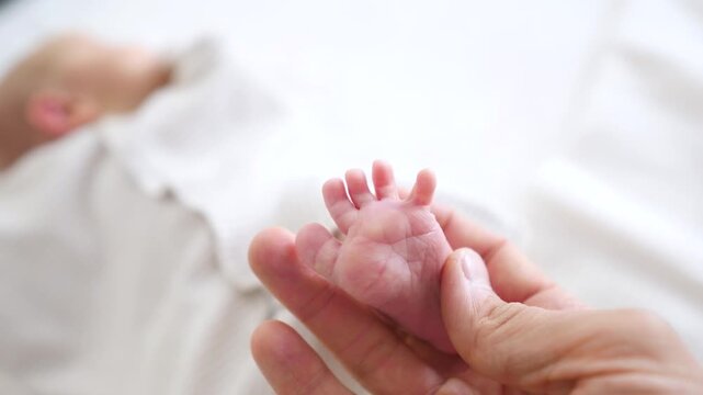 Gentle parent's hands carefully holding the tiny, delicate feet of a sleeping newborn baby, representing the concepts of family love, protection, and the beginning of a new life