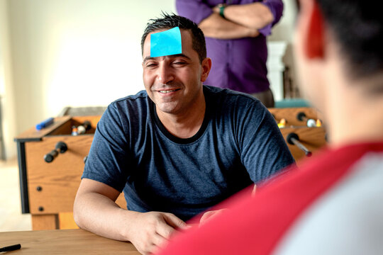 Man with sticky note on forehead, smiling, playing a guessing game.