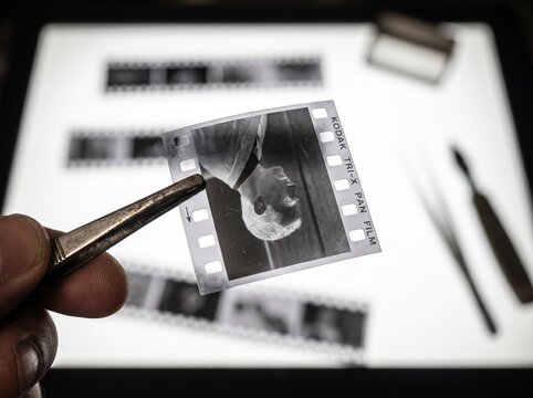 Hand holding black and white 35mm film negative over light box.