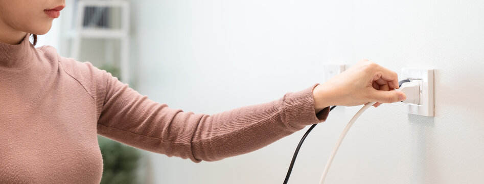 Close-up of woman hand plugging or unplugging an electrical cord into a wall socket, energy saving concept.