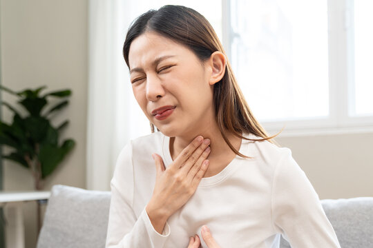 Unhappy female feeling painful with heartburn or acid reflux symptom, touching her throat and chest on sofa.