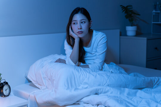 Sad unhappy female feeling worried and stressed, holding her face and awake at midnight in bedroom.