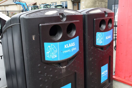 Editiorial Brown glass recycling bins with KLAAS labels in Estonian, Russian and English at an outdoor collection point near farm buildings