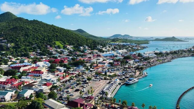 Drone view of Marigot town on the French side of Saint Martin island in the Caribbean. A vibrant waterfront with anchored boats and local markets stretches along the turquoise coastline.