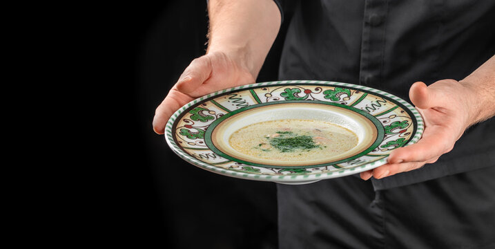 Chef serving creamy gourmet soup in decorative plate with copy space on dark background. Copy space.