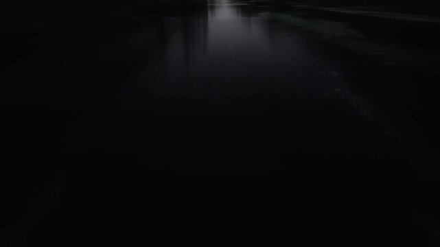 Tracking shot of canal water gliding forward with subtle ripples and reflections along dark river banks in rural night setting