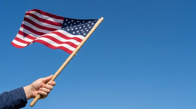 American flag held by hand against blue sky, patriotic United States flag waving in the wind, red white and blue national symbol for Fourth of July