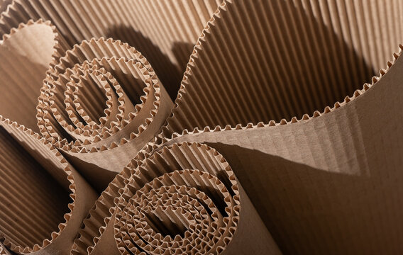 Multiple rolls of corrugated cardboard with visible wavy fluting, dramatic close-up with warm shadows. Eco-friendly kraft paper packaging material, abstract industrial texture